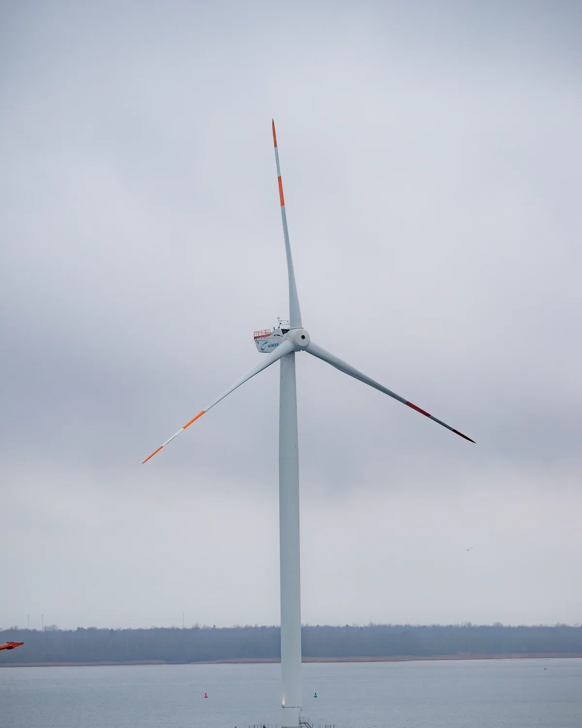 A single offshore wind turbine standing in a calm grey sea under low cloud