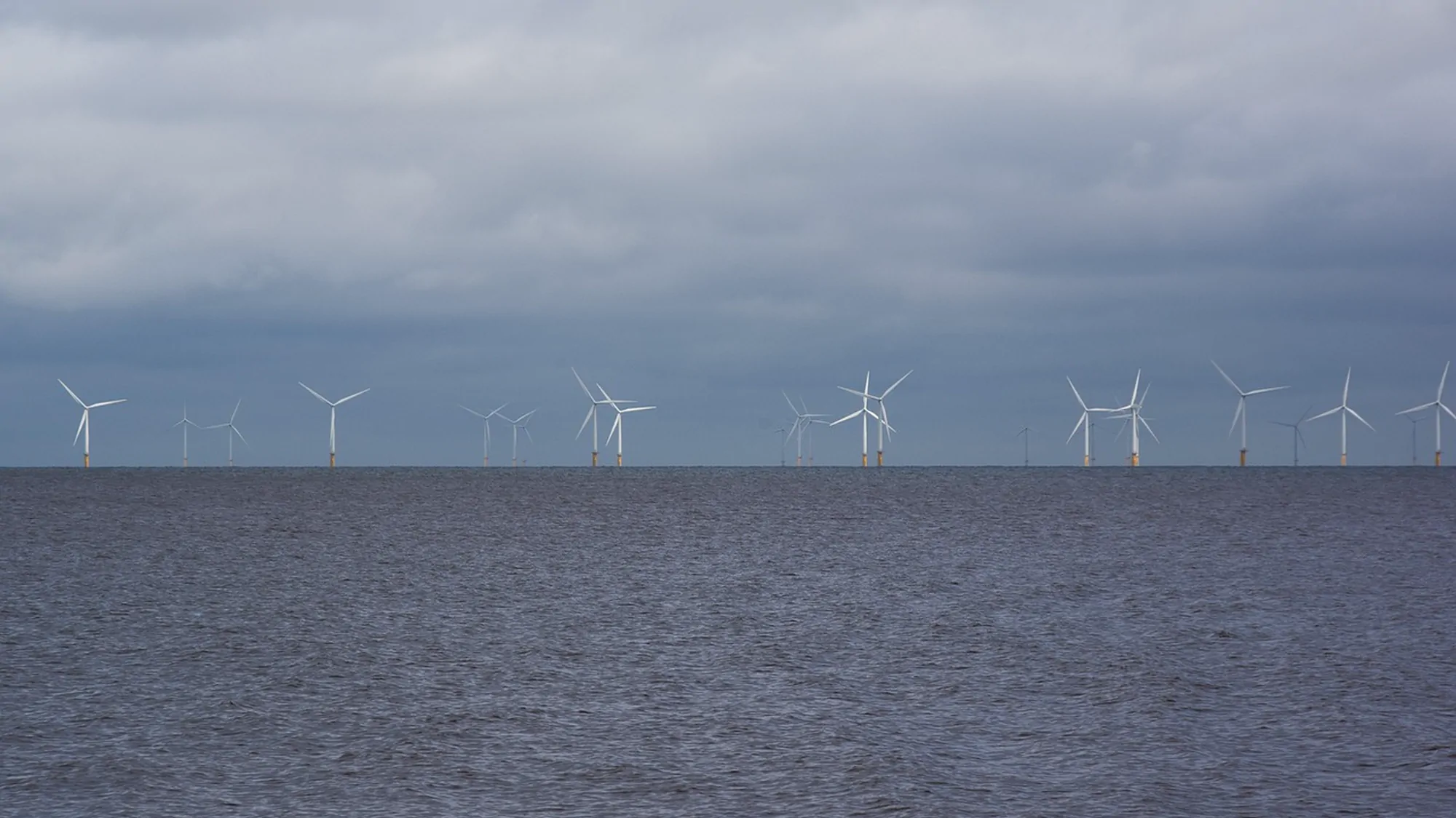A line of offshore wind turbines on the horizon under heavy grey cloud