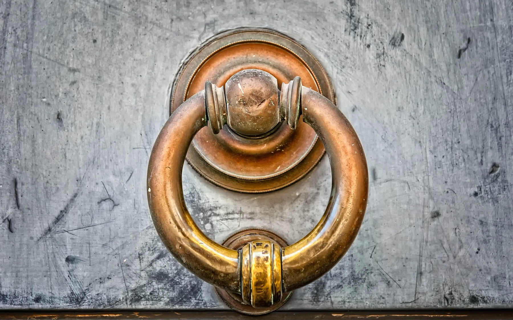 A heavy brass ring knocker on a weathered grey door
