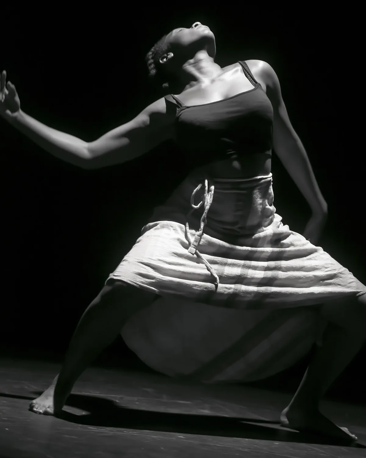 A dancer crouched low in a dark studio, lit hard from one side