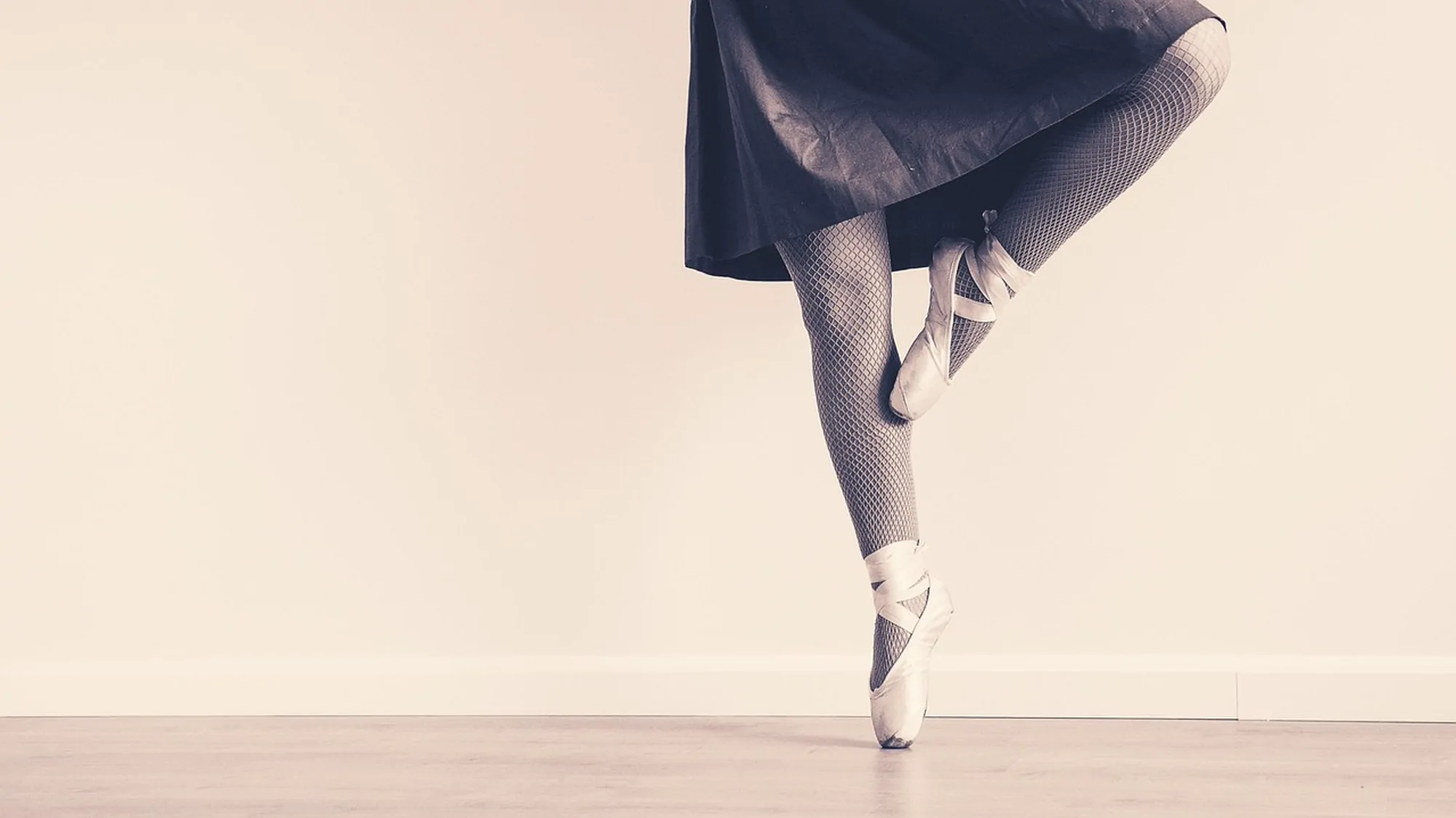 A dancer's pointe shoe and skirt against a pale studio wall