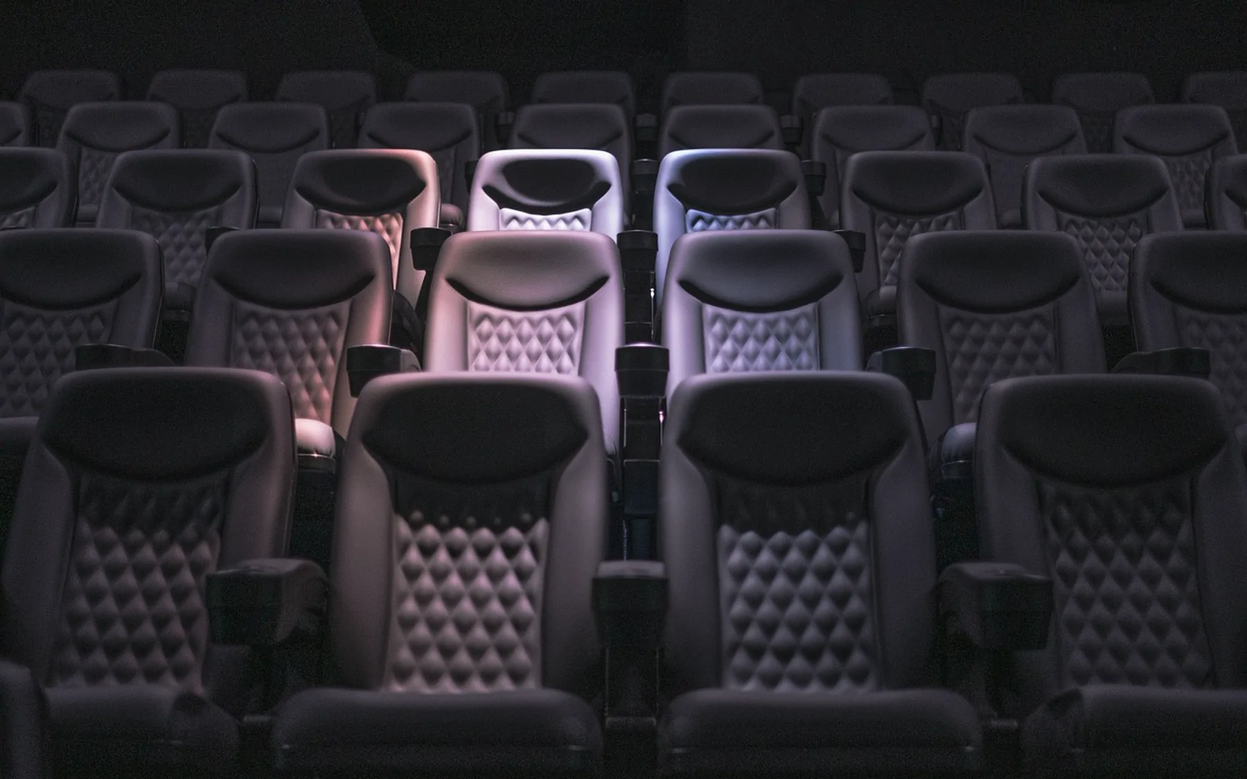Rows of empty upholstered seats in a darkened auditorium